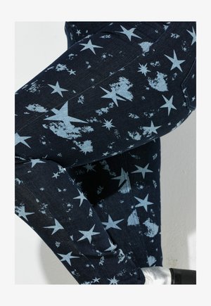 Modré džíny z denimu s hvězdicovým vzorem v světle modré barvě, se zašlým vzhledem. Detailní pohled na tkaninu a design.