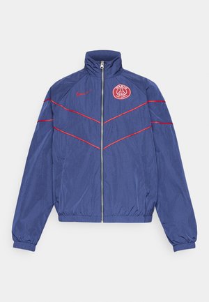 Marine vindjakke med røde detaljer, høy krage, glidelås foran og PSG-logo på venstre bryst. Elastiske mansjetter og midje for en tettsittende passform.