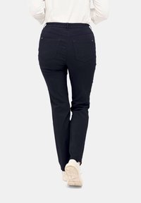 Zwarte tapered broek met een elastische tailleband en drie achterzakken, gedragen met een crème top en lichtgekleurde sneakers.