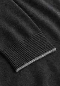 Dunkelgrauer Pulloverstoff mit einem gerippten Bündchen und einem grauen Akzent am Rand, der eine glatte Textur und ein strukturiertes Design vermittelt.