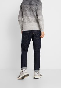 Grå ombre stickad tröja, mörka denimjeans och ljusgrå sneakers med svarta accenter. Avslappnad passform; synlig sömnad och fickdetaljer.