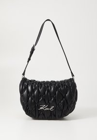 Black quilted handbag made of leather, featuring a curved shape, a slim strap, and a silver logo accent.