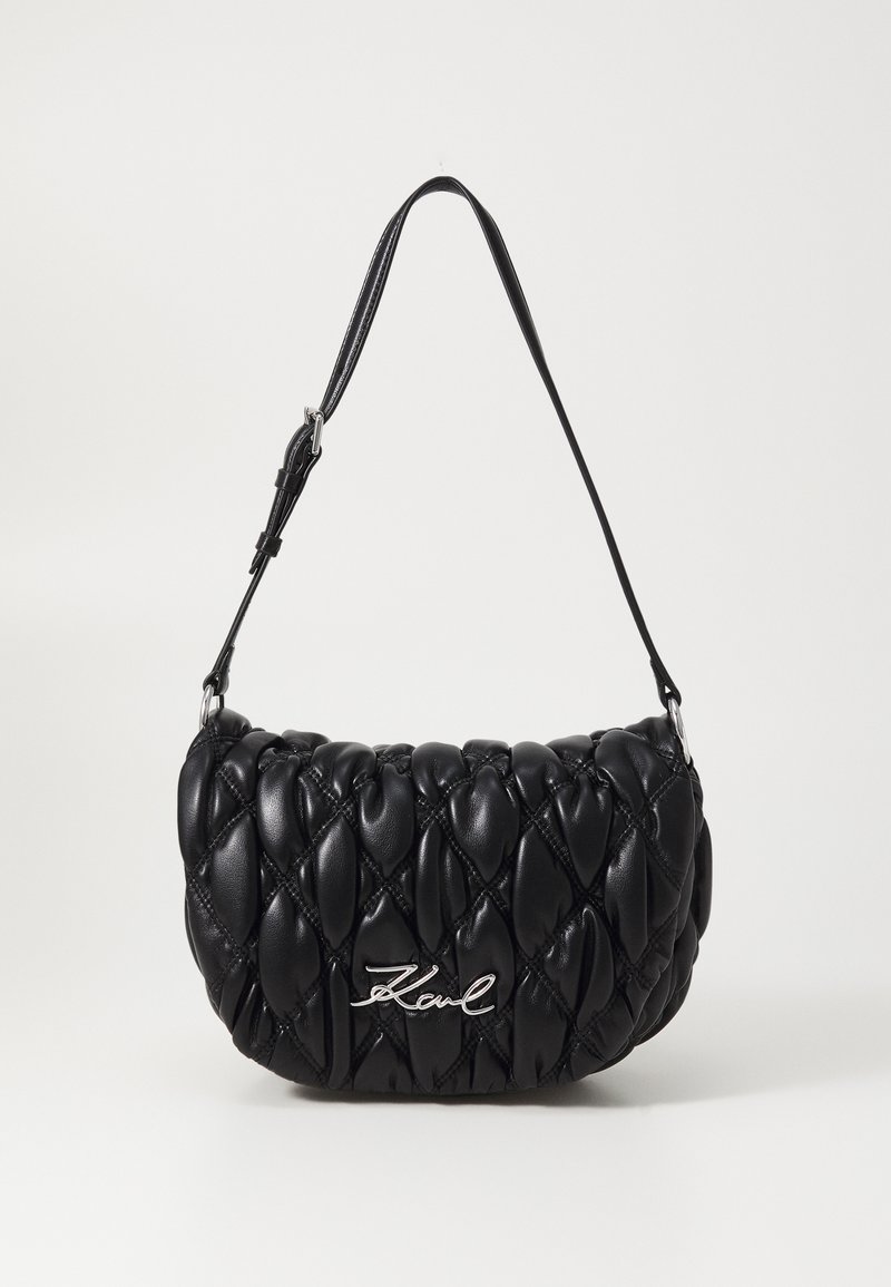 Black quilted handbag made of leather, featuring a curved shape, a slim strap, and a silver logo accent.