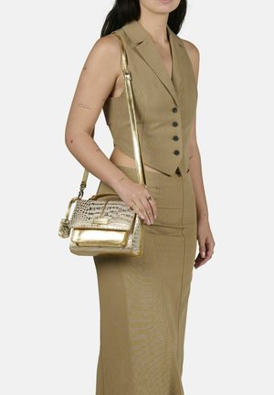 Goldene Handtasche mit Krokodilstruktur, strukturiertem Design, abnehmbarem Schulterriemen und metallischen Akzenten. Getragen mit einem passenden braunen Outfit.