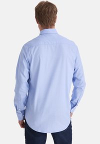 Himmelblaues Langarmshirt aus Baumwolle, mit klassischem Kragen, Knopfmanschetten und abgerundetem Saum, mit glatter Textur und minimalen Details.