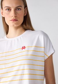 T-shirt blanc à manches courtes avec des rayures horizontales jaunes et une broderie de crabe rouge sur la poitrine. Matière en coton doux, col rond.