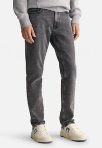 Szare dżinsy w slim fit, z klasycznym pięciopocketowym wzorem, subtelnym wybledzeniem i średnim stanem pasa. Połączone z jasnymi sneakersami.