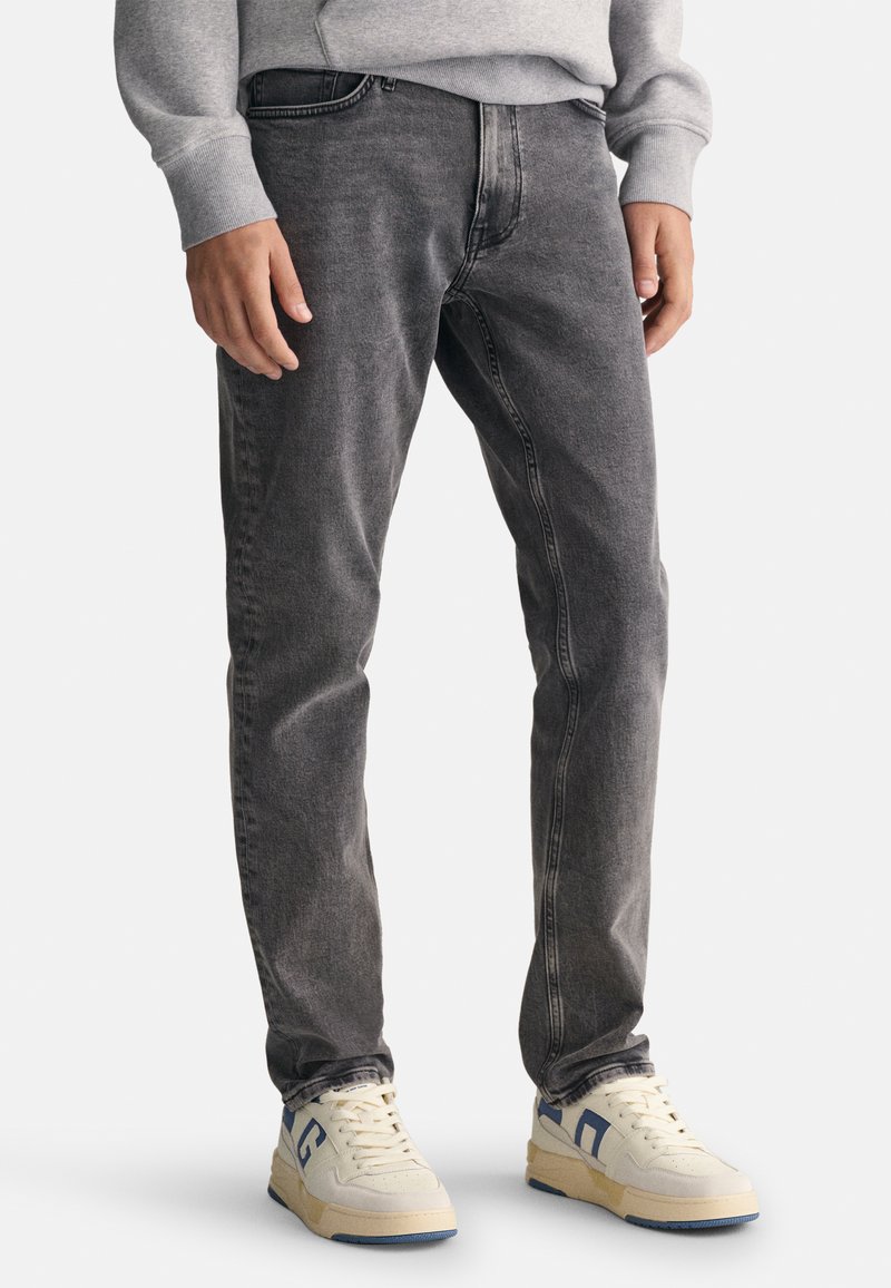 Szare dżinsy w slim fit, z klasycznym pięciopocketowym wzorem, subtelnym wybledzeniem i średnim stanem pasa. Połączone z jasnymi sneakersami.