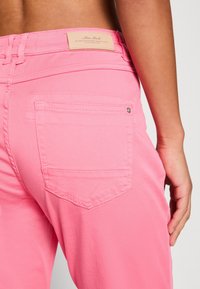 Jean en denim rose taille haute, avec des coutures contrastantes, une poche arrière munie d'un bouton métallique et une étiquette en tissu à la ceinture.