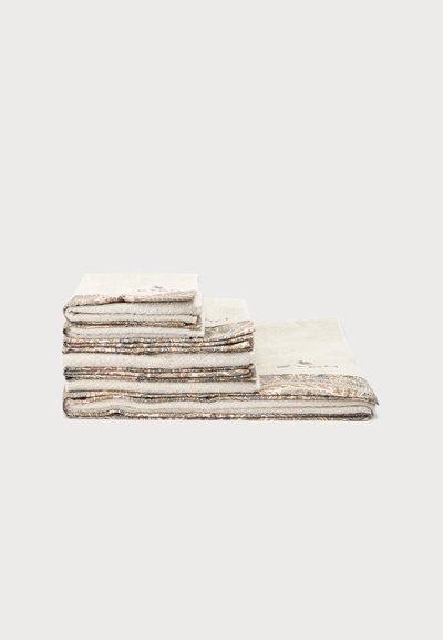Pile de serviettes beiges pliées avec des bords décoratifs à motifs sur un fond clair uni.