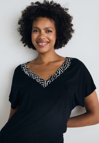 Svart t-shirt med V-ringning och en strukturerad krage i svart och vitt mönster. Mjuk, flödande tyg med korta ärmar.