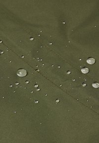 Waterbestendige groene stof met zichtbare waterdruppels, die een gladde textuur en fijne stikdetails toont.