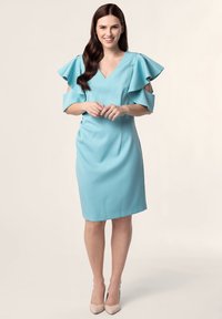 Une robe bleu clair avec un décolleté en V, des manches flottantes et un devant plissé. Tissu lisse, design midi, assortie à des talons nus.