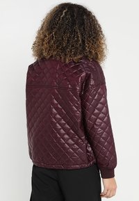 Bordeaux gekwilt jack met een glanzende afwerking, voorzien van ribbels aan de manchetten en onderrand, diamantpatroon en minimalistische ontwerp elementen.