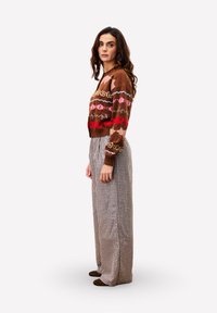 Bruin patroonsweater met roze en rode accenten, gecombineerd met bruin geruit wijde broek. Model staat in profiel.