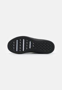 Suola di sneakers in gomma nera con un motivo testurizzato, caratterizzata da scanalature orizzontali e piccole indentazioni triangolari per il grip.