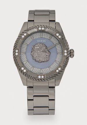 Montre Guess avec un bracelet en acier inoxydable gris, un boîtier rond, un emblème de lion, un cadran texturé bleu et des accents en cristal clair.
