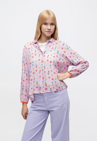 Camicia rosa chiaro con bottoni e stampa floreale, maniche lunghe e dettagli arancioni a contrasto sui polsini. Tessuto morbido e trasparente, vestibilità comoda.