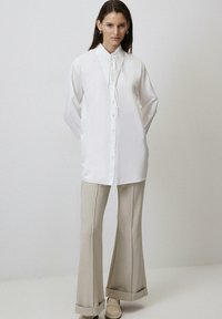 Witte blouse met lange mouwen en een strik-kraag, knoopsluiting en een gladde textuur, gecombineerd met beige flarebroeken en lichte schoenen.