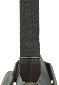 Zielony pasek torby z tkaniny o teksturowanym wykończeniu. Ciemny skórzany akcent u podstawy, z kontrastowym wykończeniem szwów. Lekka konstrukcja.