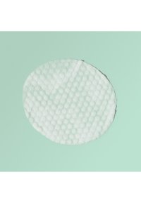 Ronde witte gestructureerde katoenen pad met verhoogd stippenpatroon op een lichtgroene achtergrond, gebruikt voor huidverzorging of make-up verwijdering.