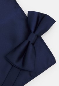 Nœud papillon en satin bleu marine avec une texture lisse, présentant un design de nœud superposé et un nœud central, sur un fond uni.