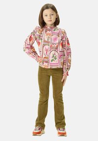 Haut à manches longues avec un motif floral coloré et du texte, associé à un pantalon en velours côtelé vert olive ; le modèle porte des baskets multicolores.