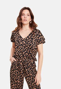 Schwarzes Oberteil mit kurzen Ärmeln, V-Ausschnitt und einem Leopardenmuster in Beige. Der Stoff wirkt weich mit einer leicht strukturierten Oberfläche.