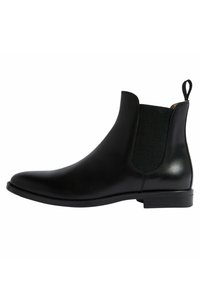Botín Chelsea de cuero negro con paneles elásticos laterales, puntera redondeada y una pequeña lengüeta. Presenta un acabado suave y un tacón bajo apilado.