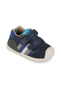 Zapato azul marino con correas de velcro, materiales de cuero y textil, rayas grises y azules en contraste, suela de goma texturizada, punta redondeada.