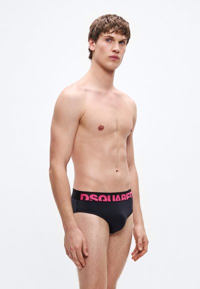 Mustad ujumispüksid laia roosa "DSQUARED2" logoga vöökohaga. Sile tekstuur, madal vöökohaga disain ja minimaalne katvus.