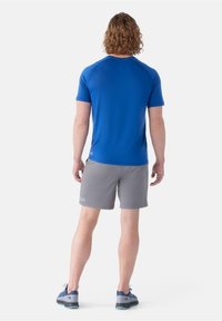 Pánský sportovní outfit obsahující modrou košili s krátkým rukávem a šedé šortky, vyrobený z lehké tkaniny, s jednoduchým a funkčním designem.