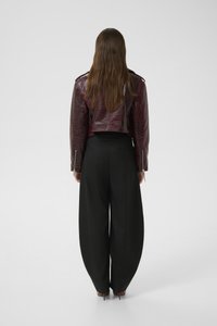 Cropped burgundy faux-crocodile leather jacket with silver hardware, paired with high-waisted black wide-leg trousers.