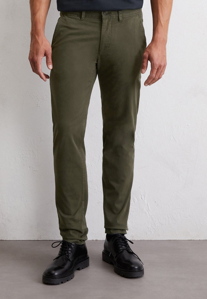 Olivgrüne Chinos mit slim fit, aus weichem Stoff. Mit Knopfverschluss und schlankem Design, kombiniert mit schwarzen Schnürstiefeln.