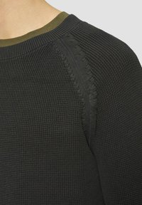 Schwarzer strukturierter Strickpullover mit rundem Ausschnitt und olivgrünem Kragen. Besitzt markante Nähte an der Schulter.