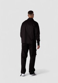 Schwarze Jacke mit lässigem Schnitt, gefütterten Manschetten und geradem Saum, kombiniert mit passenden Cargo-Hosen, die über Seitentaschen und eine glatte Textur verfügen.