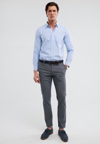 Svijetloplava košulja na dugih rukava, sivi hlače, tamnoplave cipele. Slim fit kroj s kragnom, džepom na prsima i teksturiranim remenom.