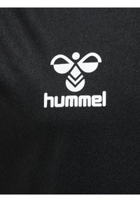 Tejido negro con un distintivo logo blanco de Hummel, que incluye una abeja estilizada y patrones geométricos. Textura suave, diseño minimalista.
