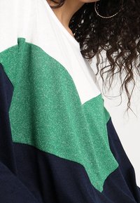 Sweter typu pulower z kolorowym wzorem w odcieniach zieleni, bieli i granatu. Wykonany z teksturowanej dzianiny, o luźnym kroju i długich rękawach.