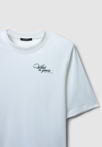 T-shirt en coton blanc avec un col rond et des manches courtes. Présente un texte brodé vert : "Ce qui est à toi te trouvera."