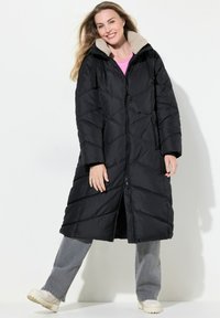 Lunga giacca a vento nera con trapuntatura a diamante, colletto foderato in pile beige, chiusura frontale con zip, tasche laterali e design morbido.