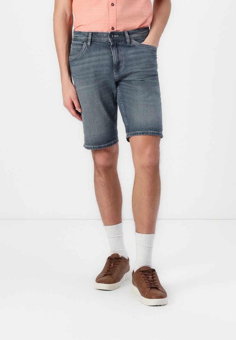 Denimshorts i en falmet blå nuance, med lige snit, opfoldede kanter, forlommer og parret med brune sneakers og hvide sokker.