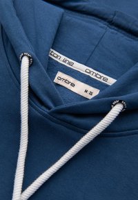 Felpa blu in cotone, dotata di un cordoncino con dettagli bianchi. Le etichette indicano la taglia M e il marchio. Texture morbida e design classico.