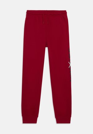 Pantalon de jogging rouge avec taille élastique, cordon, chevilles retroussées et détail de texte noir et blanc sur la jambe droite.