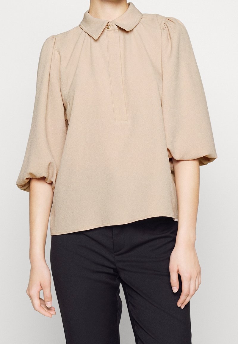 Beige, kortärmad blus med krage, knäppning framtill och veckningar vid axlarna. Mjuk, lättviktsmaterial.