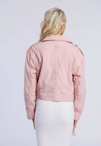 Kortad rosa läderjacka med krage, axelkapper och synliga sömmar, matchad med en vit ribbad klänning nedanför.