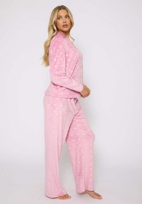 Pijamas de forro polar rosa con un patrón de corazones, mangas largas, una parte delantera abotonada y pantalones de corte holgado con cintura elástica.