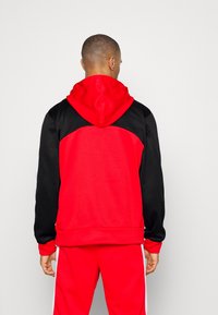 Sweat à capuche rouge et noir avec un design bicolore contrasté ; présente un tissu texturé, une poche kangourou et des poignets côtelés.