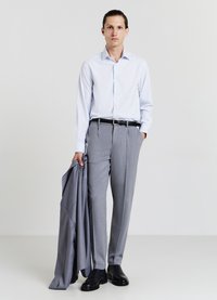 Camicia azzurra chiara a maniche lunghe, pantaloni grigi sartoriali, cintura nera e scarpe. Giacca grigia tenuta sopra il braccio sinistro. Tessuto liscio, design formale.