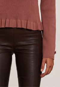 Maglione rosa a costine con orlo a balze, abbinato a pantaloni in similpelle marroni, che mettono in mostra una texture liscia e un design aderente.